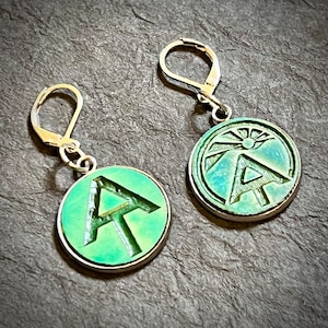 May include: A pair of silver earrings with green circular pendants. Each pendant features a raised, stylized letter "A" design.