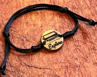May include: A black cord bracelet with a wooden charm featuring a jeep silhouette and the word "Explore".