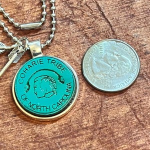 May include: A silver necklace with a round pendant featuring a green image of a Native American person's head with the text "Coharie Tribe of North Carolina".