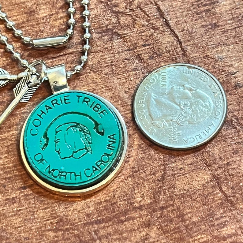 May include: A silver necklace with a round pendant featuring a green image of a Native American person's head with the text "Coharie Tribe of North Carolina".
