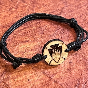 May include: A black cord bracelet with a wooden circle charm featuring a black and white arrowhead design.