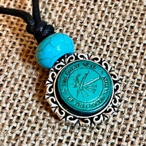 May include: A turquoise bead necklace with a silver pendant featuring the Great Seal of the State of Oregon. The seal depicts a green evergreen tree with a beaver gnawing on a branch.