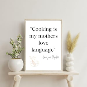 May include: A white framed print with a black quote that reads "Cooking is my mothers love language" with a small illustration of a whisk in a bowl and the text "Love, your Daughter".