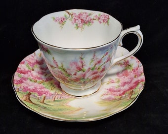 May include: A white teacup and saucer set with a floral pattern of pink blossoms and green leaves. The cup and saucer have a gold trim.