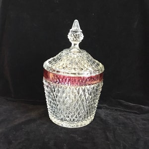 May include: A clear glass candy dish with a diamond pattern and a red band around the top. The lid has a pointed finial.