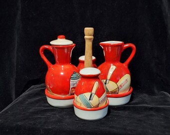 May include: A set of four red ceramic condiment bottles with white lids and a wooden dispenser. The bottles are decorated with images of various cheeses and the words "Cheddar", "Swiss", "Pepper Jack", and "Provolone".