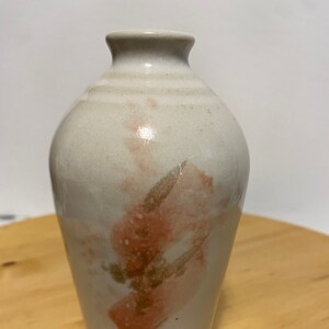 May include: A handmade ceramic vase with a cream base and a narrow neck. The vase features abstract brushstrokes in coral and brown. The vase is approximately 18 cm tall and is suitable for displaying flowers or as a decorative piece.