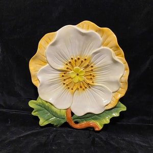 May include: A white ceramic flower-shaped serving dish with yellow and green accents. The dish is shaped like a large flower with a centre of yellow and brown dots.