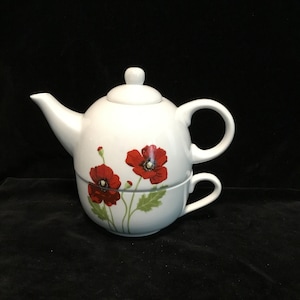 May include: White porcelain teapot and cup set with a floral design featuring red poppies. The teapot has a lid and a handle, and the cup has a handle.