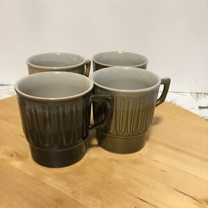 May include: Set of four ceramic mugs with a brown and grey glaze. The mugs have a ribbed design and a rounded shape.