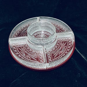 May include: A clear glass divided serving platter with a central circular bowl and four surrounding wedge-shaped compartments. The glass features intricate pressed patterns including radiating sunburst motifs and cross-hatch diamond textures.