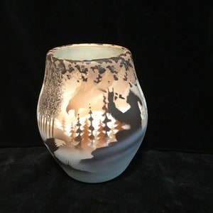 Peut inclure: Un vase en céramique avec un glaçage brun et blanc. Le vase présente un motif en silhouette d'arbres, d'oiseaux et d'un ours dans un décor de forêt.