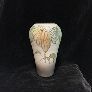 May include: A tapered ceramic vase with a matte off-white finish, featuring hand-painted illustrations of large, veined leaves in shades of muted yellow, sage green, and charcoal grey. The design wraps around the upper body of the vessel.