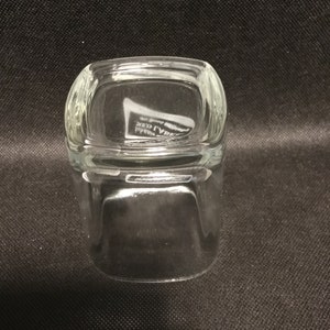 Op de afbeelding: Een helder glazen tumbler met een vierkante vorm en afgeronde randen. De bodem van het glas heeft de tekst "RED LABEL" erin gegraveerd.