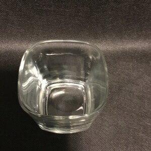 Op de afbeelding: Een transparante glazen tumbler met een vierkante vorm. Het glas is leeg en heeft een lichte kromming aan de zijkanten.
