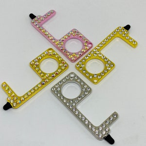 Puede incluir: Cuatro abridores de puertas con pedrería. Los abridores de puertas son de color rosa, dorado y plateado. Cada abridor tiene una punta de estilete en un extremo y un bucle en el otro.