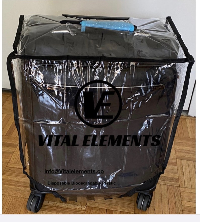 May include: A clear plastic luggage cover with a black trim and a black Vital Elements logo. The cover is over a black suitcase with wheels. The text "info@vitalelemets.co" and "Disposable Biodegradable Plastic" is printed on the cover.