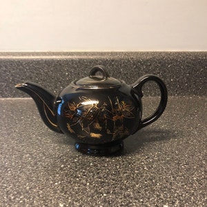 May include: A black teapot with gold floral and bamboo designs. The teapot has a round body and a small spout.