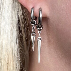 Puede incluir: Pendientes de aro plateados con colgantes c&oacute;nicos. Los pendientes son de metal brillante y se llevan en la oreja. El dise&ntilde;o es sencillo pero llamativo, adecuado para diferentes estilos. Los colgantes miden unos 2,5 cm.