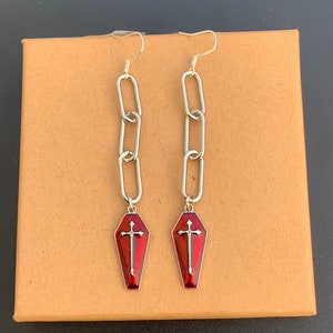 The coffin charms have a silver outline. In the centre of the charms, there is also a large silver cross. The rest of the coffin charm is red. It is a multi-tonal red and reflects light beautifully.