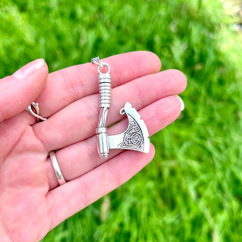 May include: Silver axe pendant with a Celtic knot design on the blade. The axe is on a silver chain.