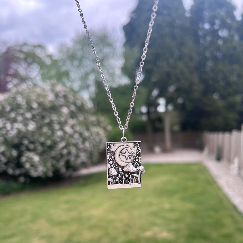 Another image of the mushroom necklace dangling freely against a green grass background.