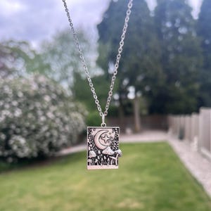 The mushroom necklace is dangling in the centre of the image. The background is green grass. This image is taken in natural daylight to best represent what the charm looks like.