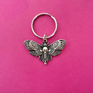 May include: A silver key chain with a detailed moth charm featuring a skull design. The moth has intricate wings and a black skull in the center.