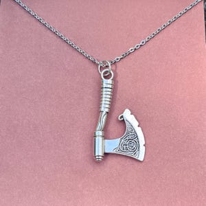 May include: A silver necklace with a detailed axe pendant. The axe has a Celtic knot design on the blade.