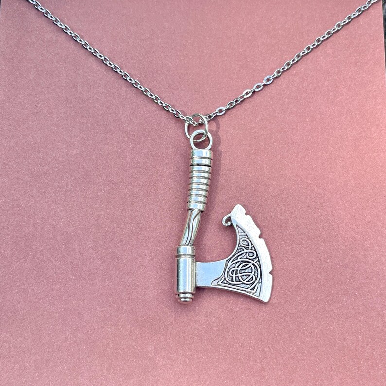 May include: A silver necklace with a detailed axe pendant. The axe has a Celtic knot design on the blade.