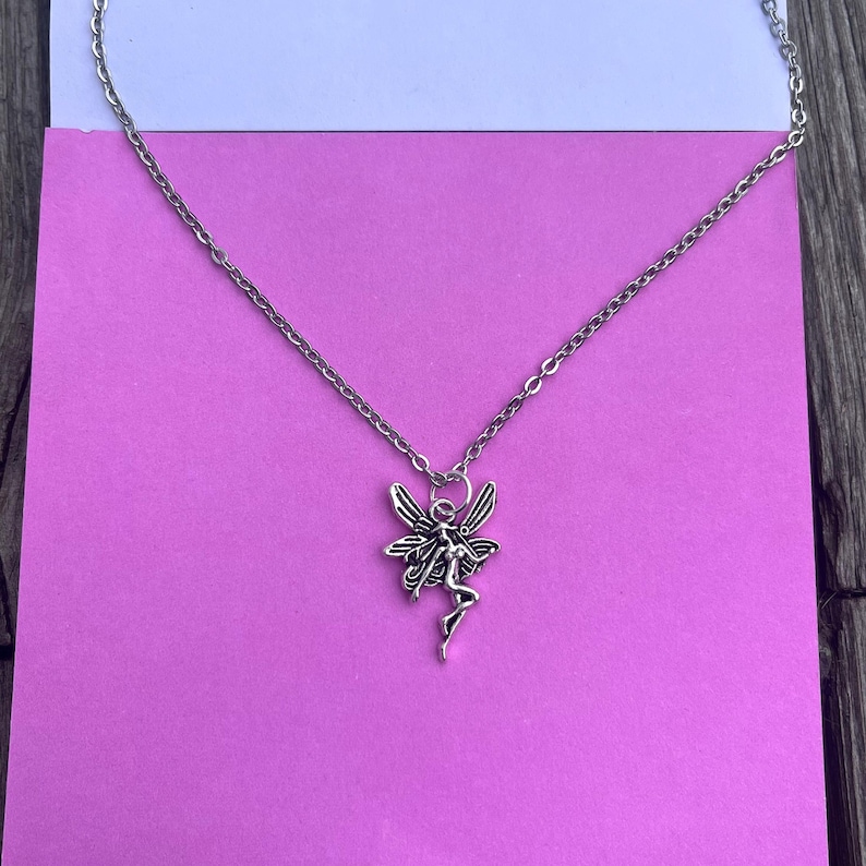 Another image of the fairy necklace placed against a pink background.