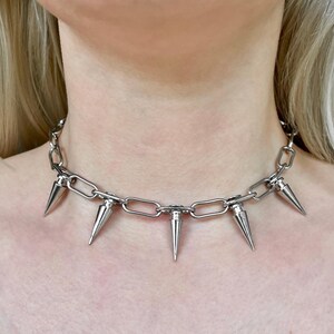 Puede incluir: Un collar de cadena plateada con m&uacute;ltiples puntas c&oacute;nicas. El collar, hecho de piezas de metal unidas, se lleva alrededor del cuello. Las puntas est&aacute;n espaciadas uniformemente a lo largo de la cadena.