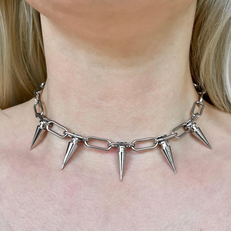 Puede incluir: Un collar de cadena plateada con m&uacute;ltiples puntas c&oacute;nicas. El collar, hecho de piezas de metal unidas, se lleva alrededor del cuello. Las puntas est&aacute;n espaciadas uniformemente a lo largo de la cadena.