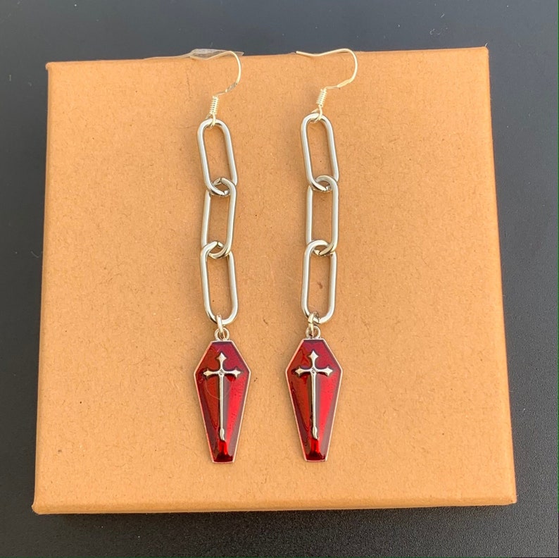 The coffin charms have a silver outline. In the centre of the charms, there is also a large silver cross. The rest of the coffin charm is red. It is a multi-tonal red and reflects light beautifully.