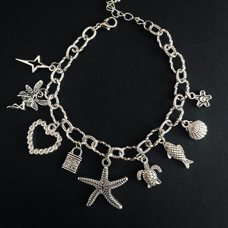 May include: Silver-toned charm bracelet featuring various pendants, including a starfish, heart, turtle, and seashell. The bracelet has a chain link design and a lobster clasp closure. The charms are detailed and add a whimsical touch.