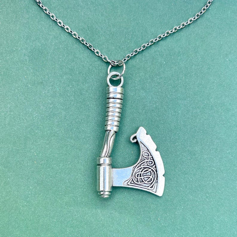 May include: A silver necklace with a detailed axe pendant. The axe has a twisted handle and a Celtic knot design on the blade.