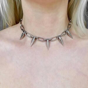 Puede incluir: Collar de cadena plateada con m&uacute;ltiples p&uacute;as c&oacute;nicas. El collar tiene un dise&ntilde;o de cadena gruesa con p&uacute;as espaciadas uniformemente, creando una est&eacute;tica audaz y vanguardista. El metal tiene un acabado pulido y reflectante.