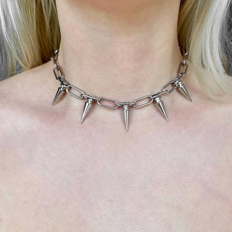 Puede incluir: Collar de cadena plateada con m&uacute;ltiples p&uacute;as c&oacute;nicas. El collar tiene un dise&ntilde;o de cadena gruesa con p&uacute;as espaciadas uniformemente, creando una est&eacute;tica audaz y vanguardista. El metal tiene un acabado pulido y reflectante.
