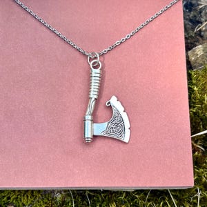May include: A silver necklace with a detailed axe pendant. The axe has a Celtic knot design on the blade.