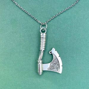 May include: A silver necklace with a detailed axe pendant. The axe has a Celtic knot design on the blade.