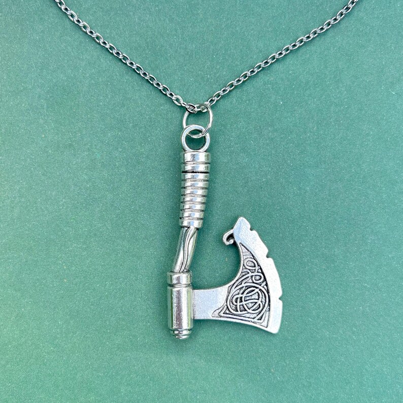 May include: A silver necklace with a detailed axe pendant. The axe has a Celtic knot design on the blade.