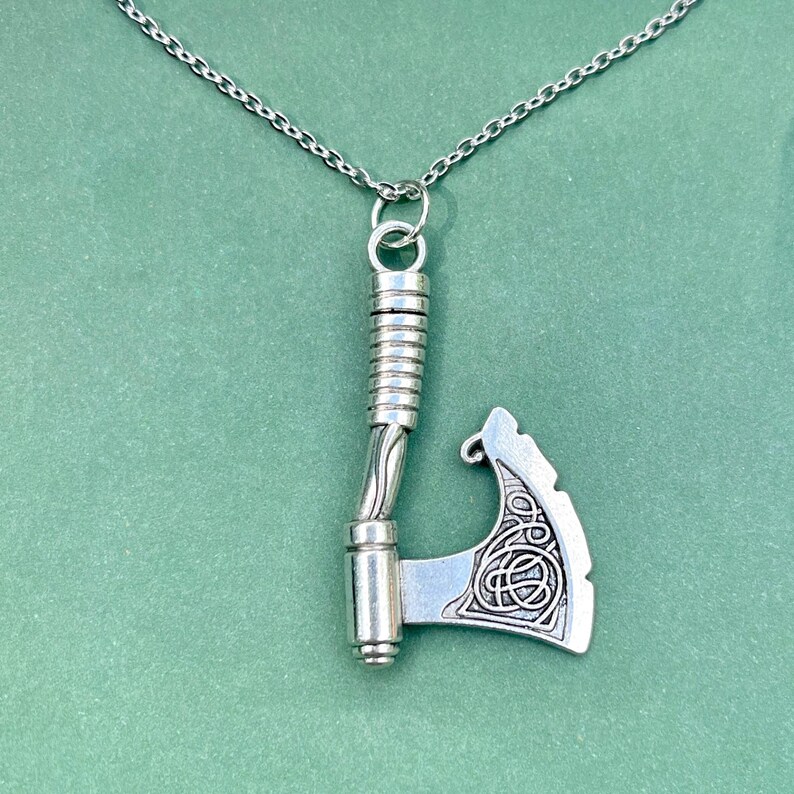 May include: A silver necklace with a detailed axe pendant. The axe has a twisted handle and a Celtic knot design on the blade.