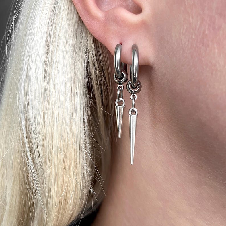 Puede incluir: Pendientes de aro plateados con colgantes c&oacute;nicos. Los pendientes son de metal brillante y se llevan en la oreja. El dise&ntilde;o es sencillo pero llamativo, adecuado para diferentes estilos. Los colgantes miden unos 2,5 cm.