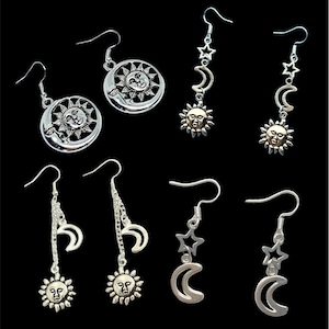 May include: Set of six silver earrings featuring celestial designs. Each earring features a crescent moon and a sun with a face. Some earrings have a dangling chain with a star charm.