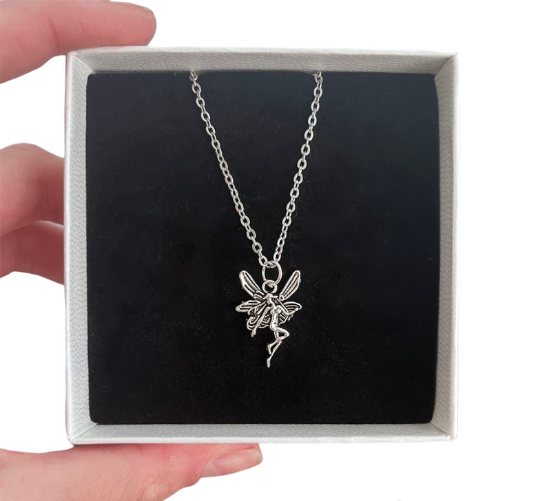 The fairy pendant has four large wings. The fairy wings have black lines on them to create definition and texture. The fairy is looking to the left and has both arms out. One leg is bent so it looks like the fairy is dancing.