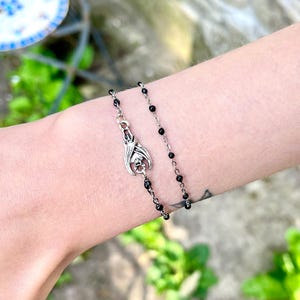 Peut inclure: Un bracelet &agrave; breloques chauve-souris argent&eacute; avec des perles noires. Le charm chauve-souris est orn&eacute; d'ailes et d'un cr&acirc;ne. Le bracelet est port&eacute; sur un poignet, mettant en valeur les bijoux gothiques.