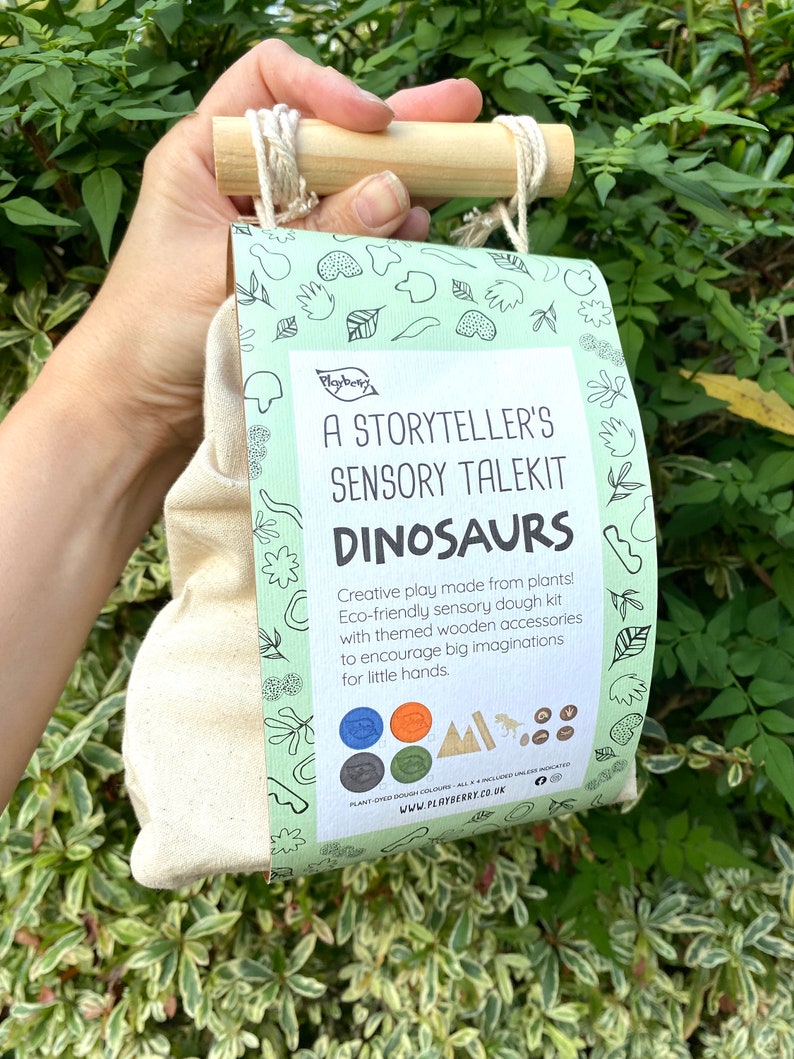 K&ouml;nnte beinhalten: Eine gr&uuml;n-wei&szlig;e Tasche mit einem Holzgriff. Die Tasche hat ein Etikett mit der Aufschrift "A Storyteller's Sensory Talekit Dinosaurs". Auf dem Etikett steht auch "Creative play made from plants! Eco-friendly sensory dough kit with themed wooden accessories to encourage big imaginations for little hands."