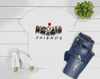 May include: White t-shirt featuring a graphic of horror movie characters with the word "FRIENDS" in black. The image includes a pair of white sneakers, blue jeans, and a small green plant on a white wooden surface.
