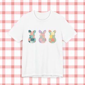 Könnte beinhalten: Weißes T-Shirt mit drei bunten Patchwork-Hasen-Designs. Jeder Hase besteht aus verschiedenen Stoffmustern in Blau-, Rosa-, Gelb- und Grüntönen. Das T-Shirt hat einen Rundhalsausschnitt und kurze Ärmel, ideal für den Alltag.