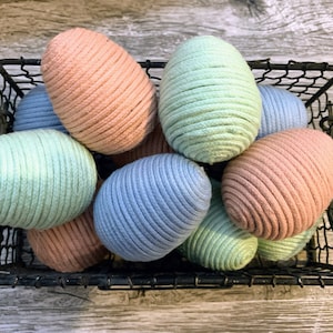 May include: A wire basket filled with pastel-colored rope Easter eggs. The eggs are in shades of blue, green, and pink.